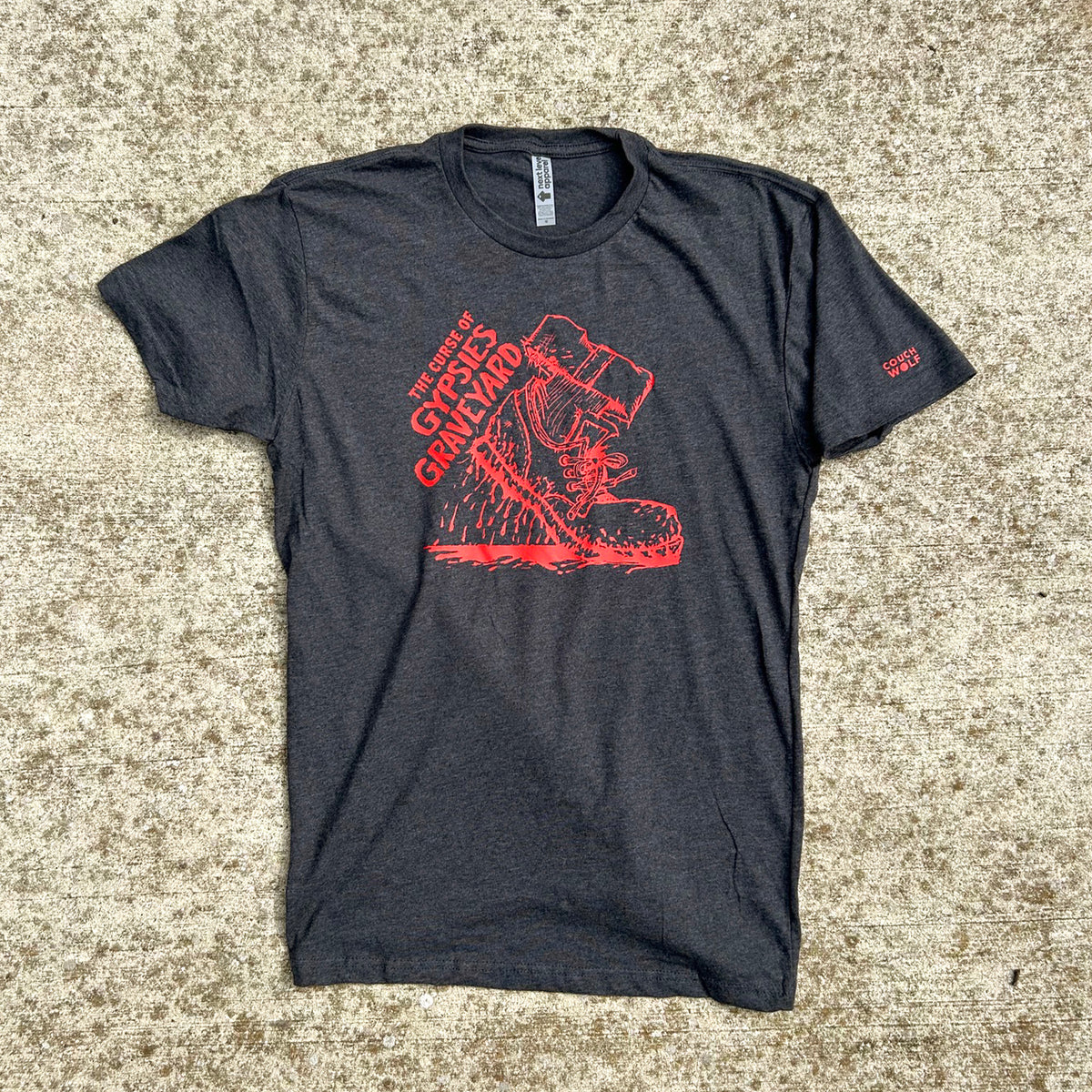 Dark heather gray t-shirt featuring a bold red graphic print of a shoe dripping blood and the text 'THE CURSE OF GYPSYS GRAVEYARD' shown on tan speckled concrete background.