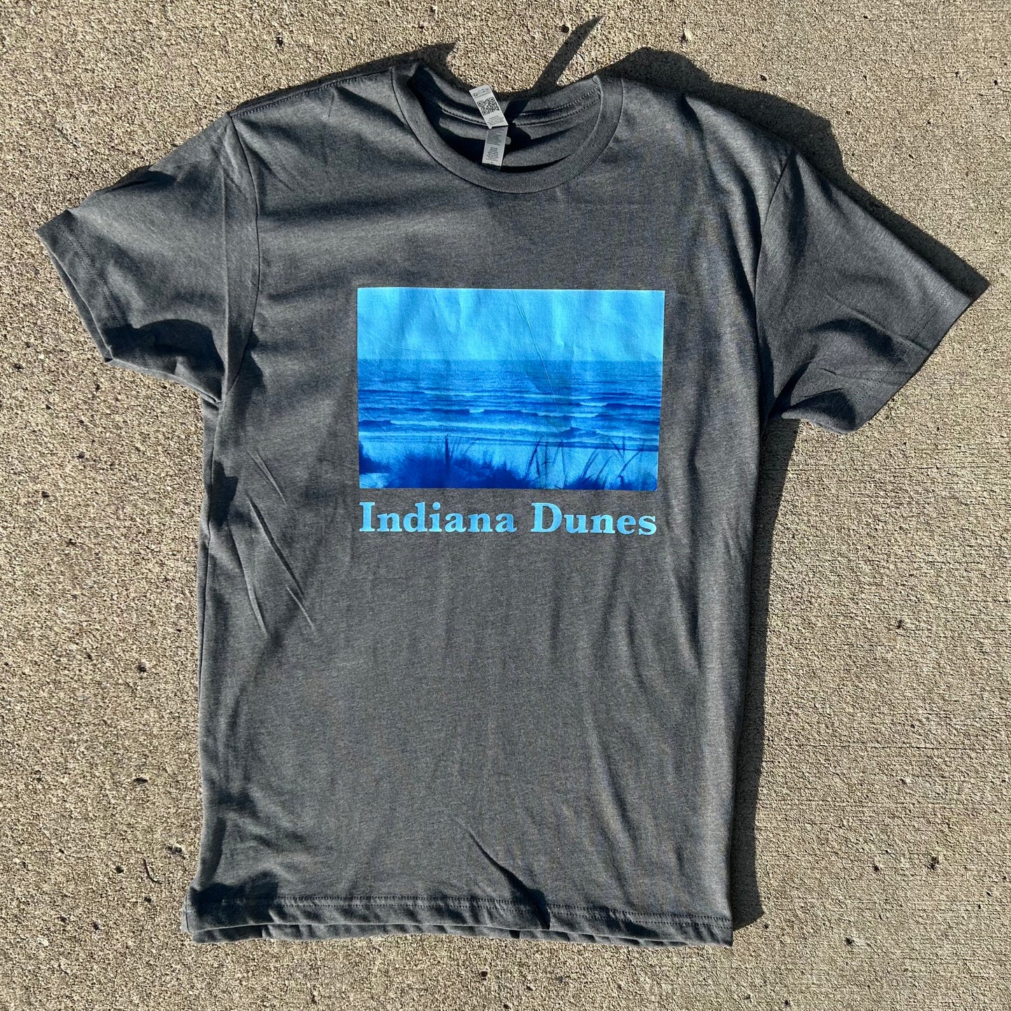 Indiana Dunes Shirt Indiana Dunes Photography t-shirt bright dark gray shirt with bright blue duotone photo of indiana Dunes National Park beach descending into lake michigan shirt on concrete brown background heavy shadows