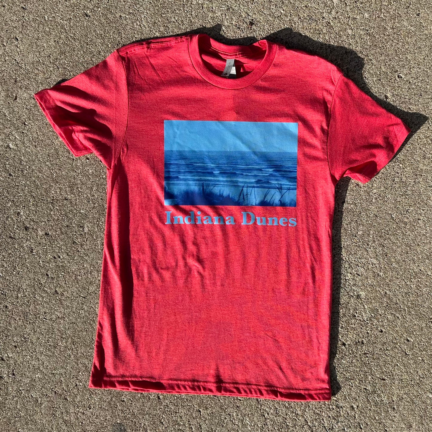 Indiana Dunes Shirt Indiana Dunes Photography t-shirt bright red heather shirt with bright blue duotone photo of indiana Dunes National Park beach descending into lake michigan shirt on concrete brown background