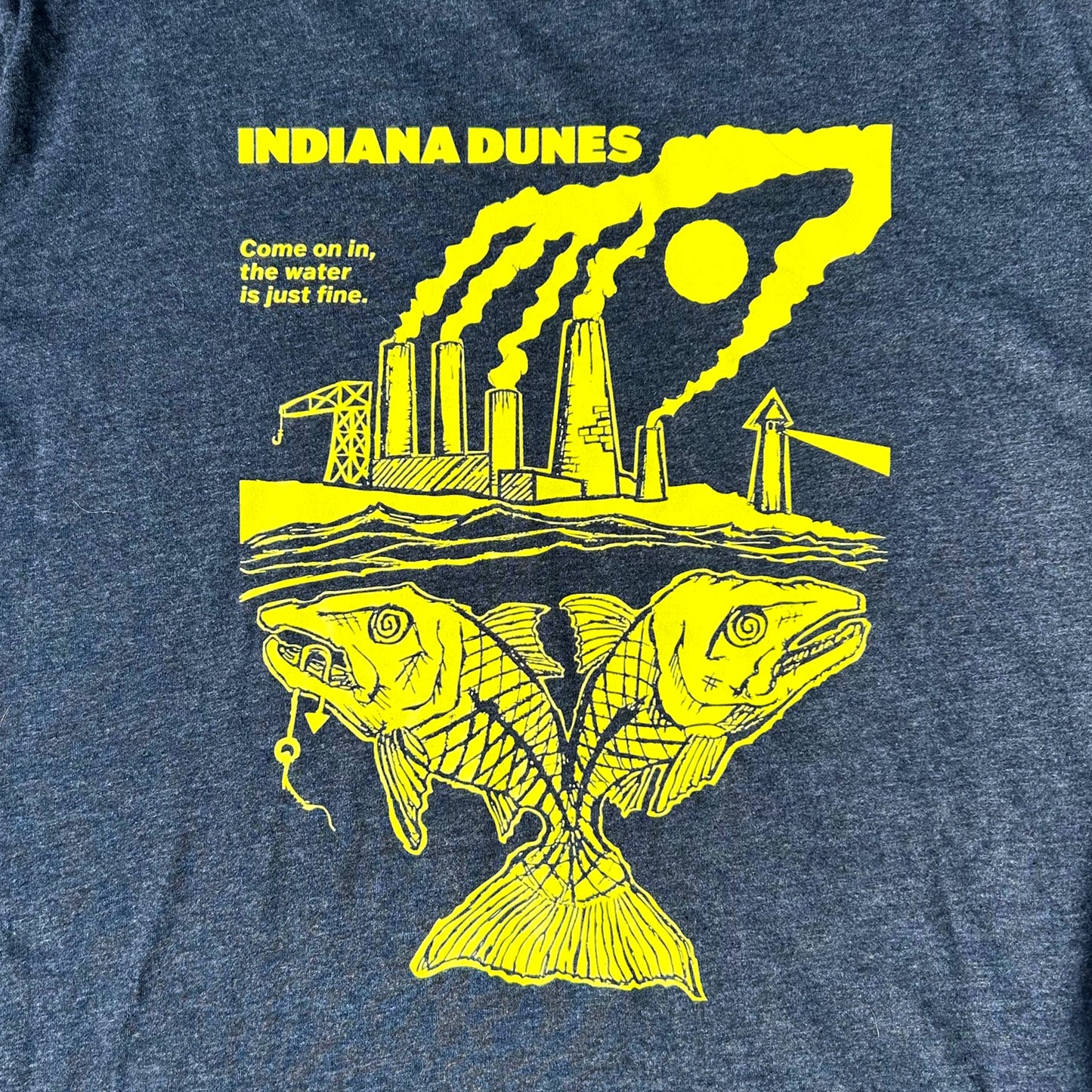 Blue t-shirt with yellow graphic of a factory and fish, featuring text 'INDIANA DUNES' and 'Come on in, the water is just fine'.