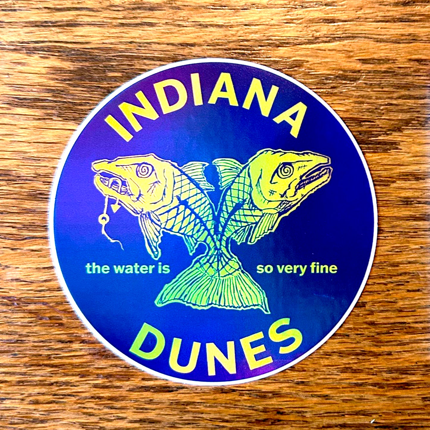 Sticker with fish illustration and 'Indiana Dunes' text on a wooden surface