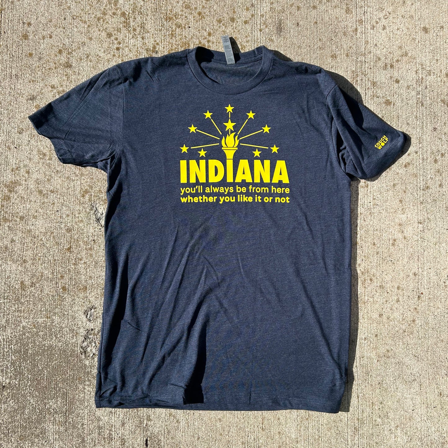 Indiana Flag T-shirt navy blue shirt with yellow bold letters that say "indiana you'll always be from here whether you like it or not" short sleeve shirt shown on tan concrete background