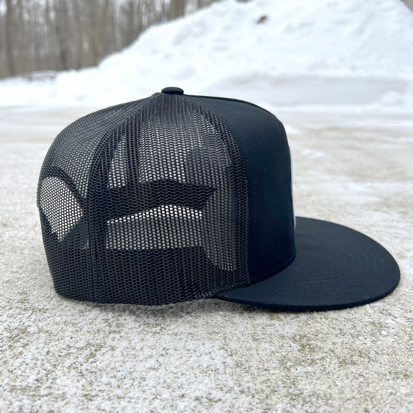 Black mesh cap on a snowy ground with trees in the background