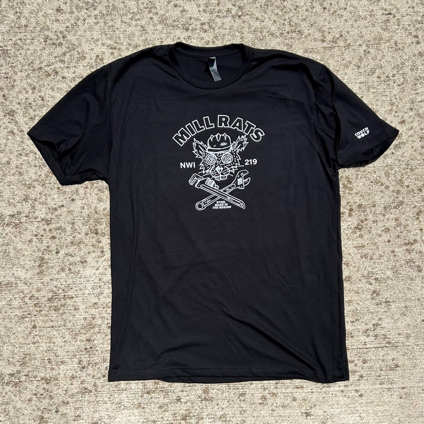 Black Mill Rats T-shirt with artwork of a rat in hard hat and 2 wrenches forming an X, printed in white ink shirt that says "Mill Rats NWI 219 Steel made in the Region", shirt is shown on beige concrete background
