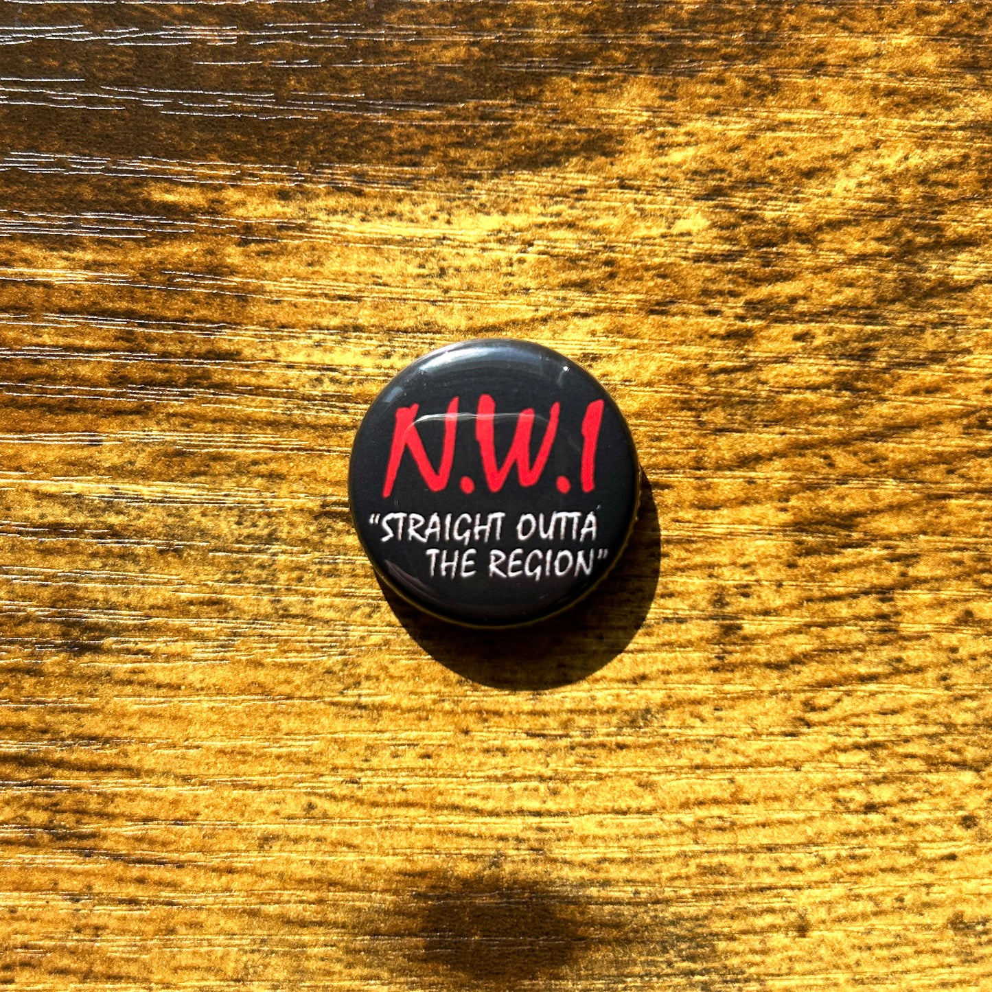 A pin with the text 'NWI Straight Outta THE REGION' on a wooden surface.
