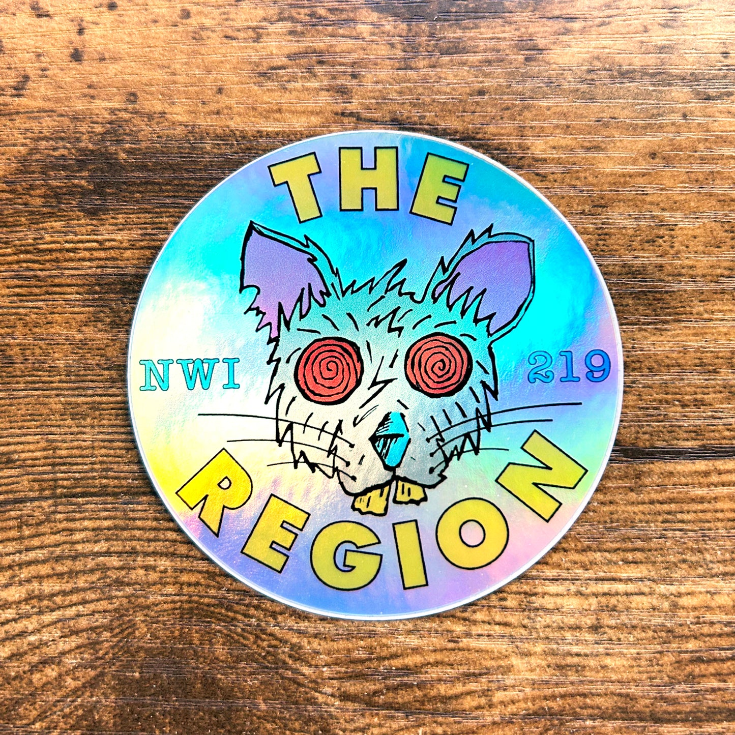 region rat sticker northwest indiana Region Rat sticker the region indiana sticker Shiny hologram region rat indiana sticker says "the region nwi 219" features psyhco red eye rat artwork black lines yellow the region tex circle sticker on wood floor background region rat head image on sticker