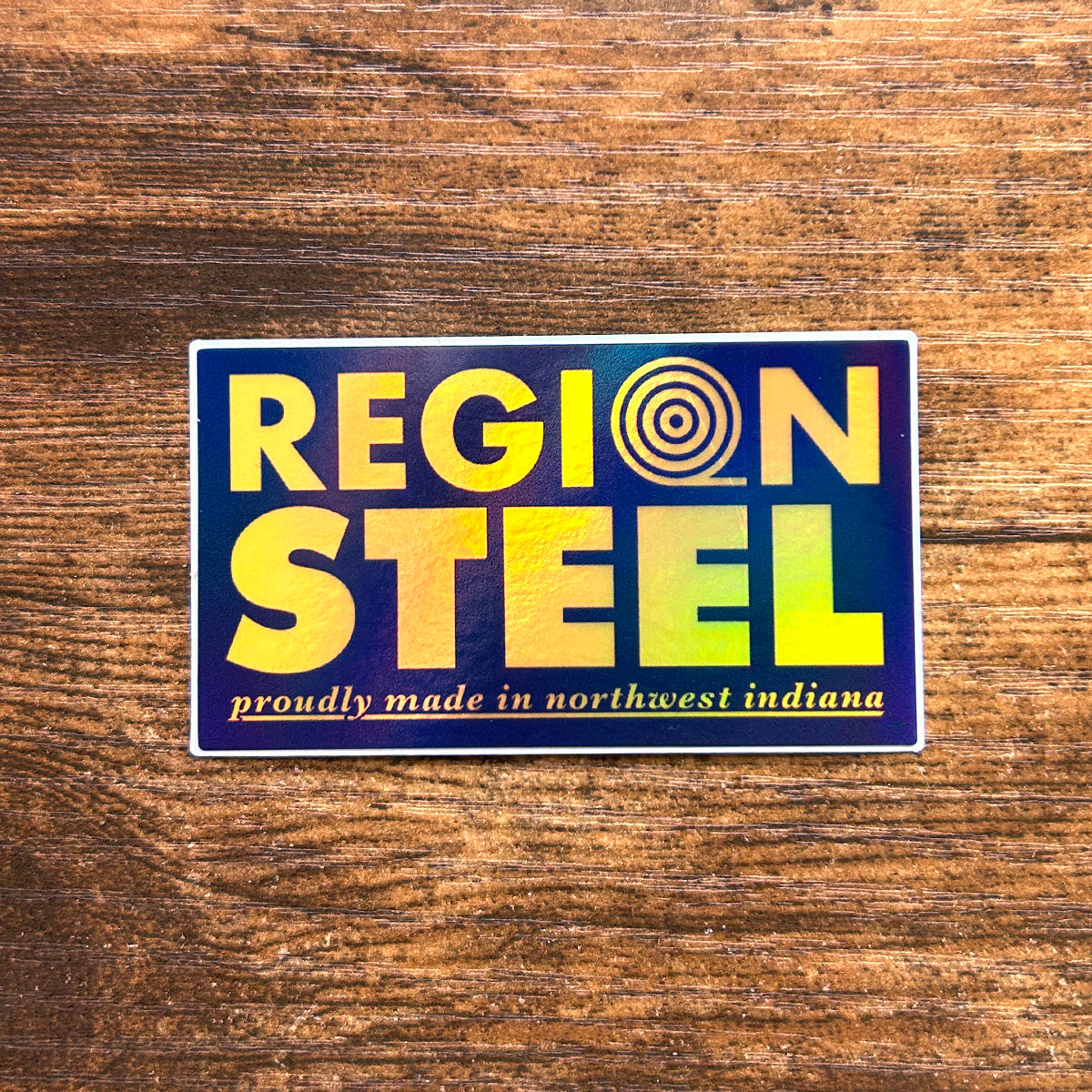 A rectangular hologram sticker with 'REGION STEEL' written on it, featuring a colorful, shiny design with text that reads 'Region Steel proudly made in northwest Indiana.'.