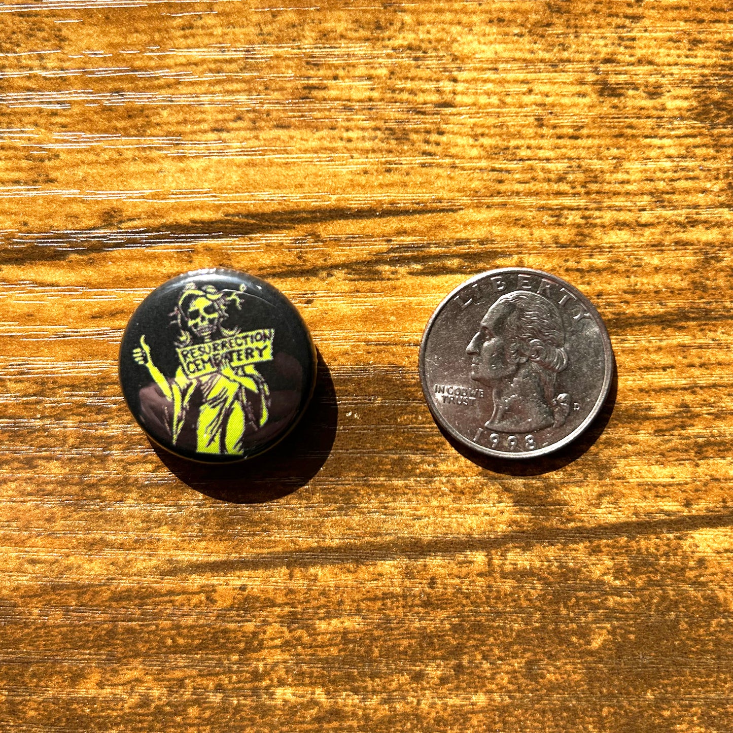 Resurrection Mary pin round black pin with green skull faced ghost art shown on wood table next to quarter