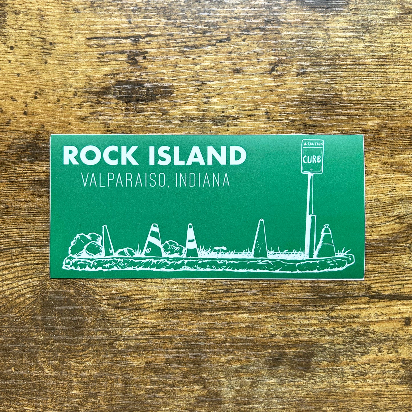Rock Island Valparaiso Indiana Sticker green sticker with white line art of parking island rocks and road cones says "Rock Island Valparaiso Indiana" shown on wood background