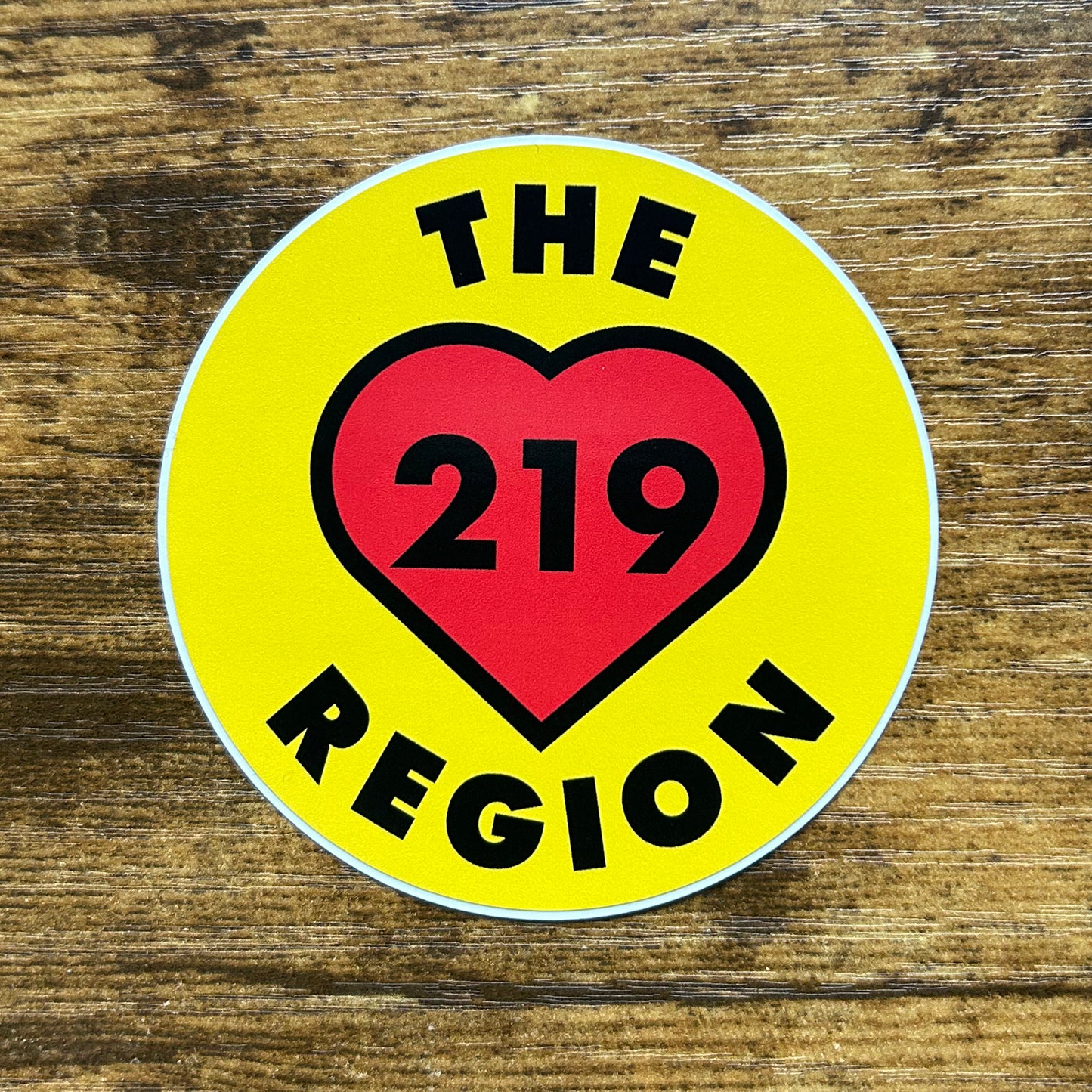 A circular sticker with a yellow background and a red heart in the center, containing the text 'THE REGION 219'.
