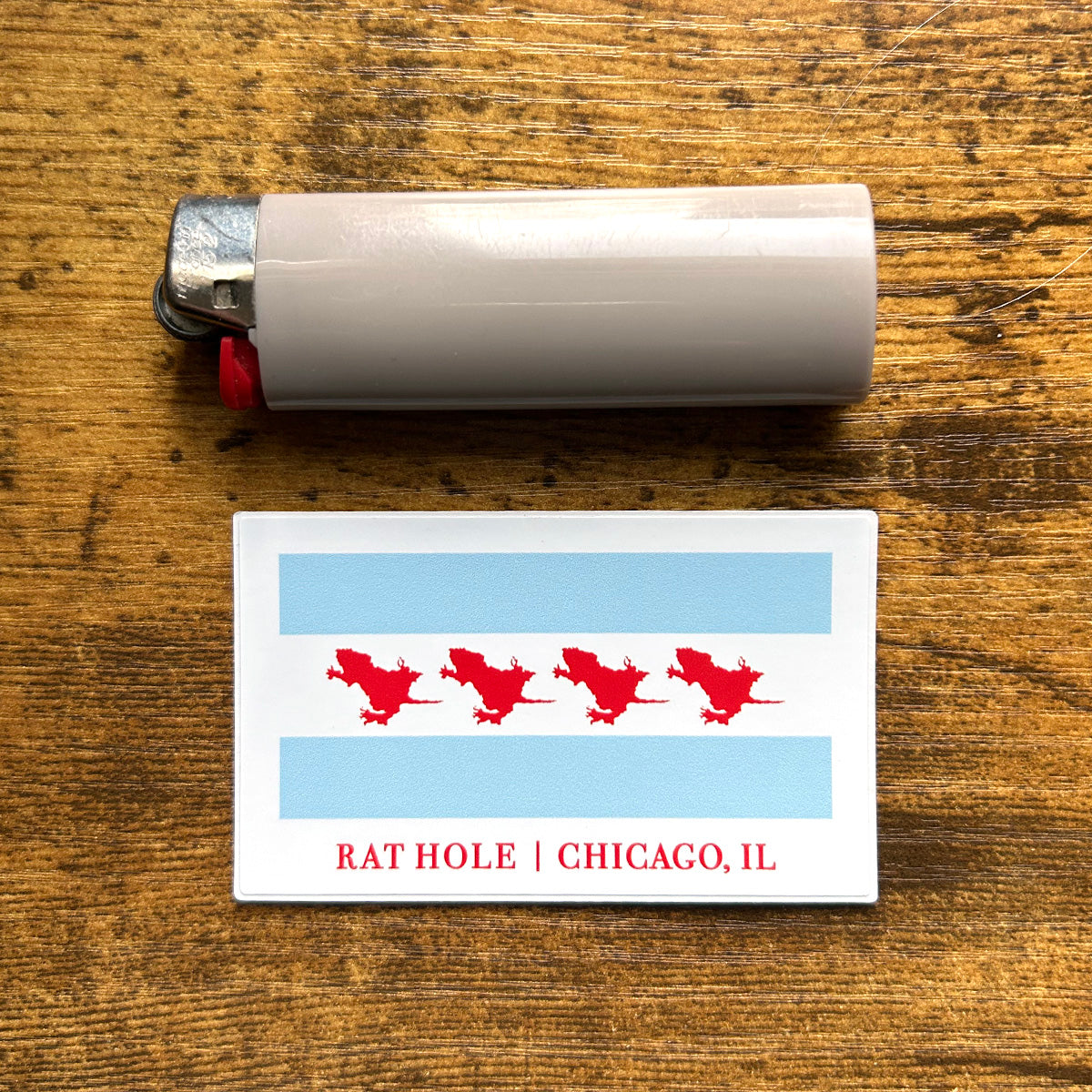 Rat Hole sticker rectangle sticker of chicago flag on wood background next to gray disposable lighter