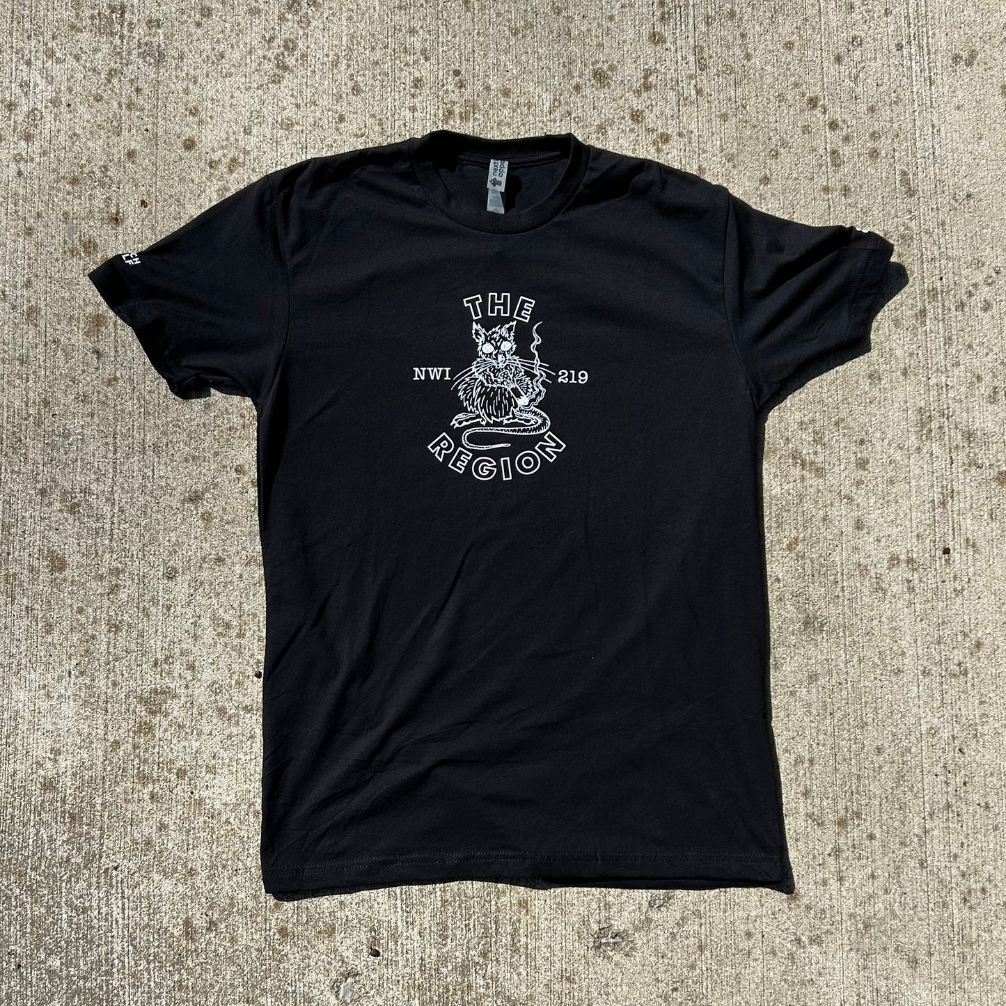 The Region Indiana t-shirt region rat t shirt black short sleeve shirt with white ink region rat artwork smoking a cigarette says The Region NWI 219 art by couch wolf shirt shown on tan concrete background
