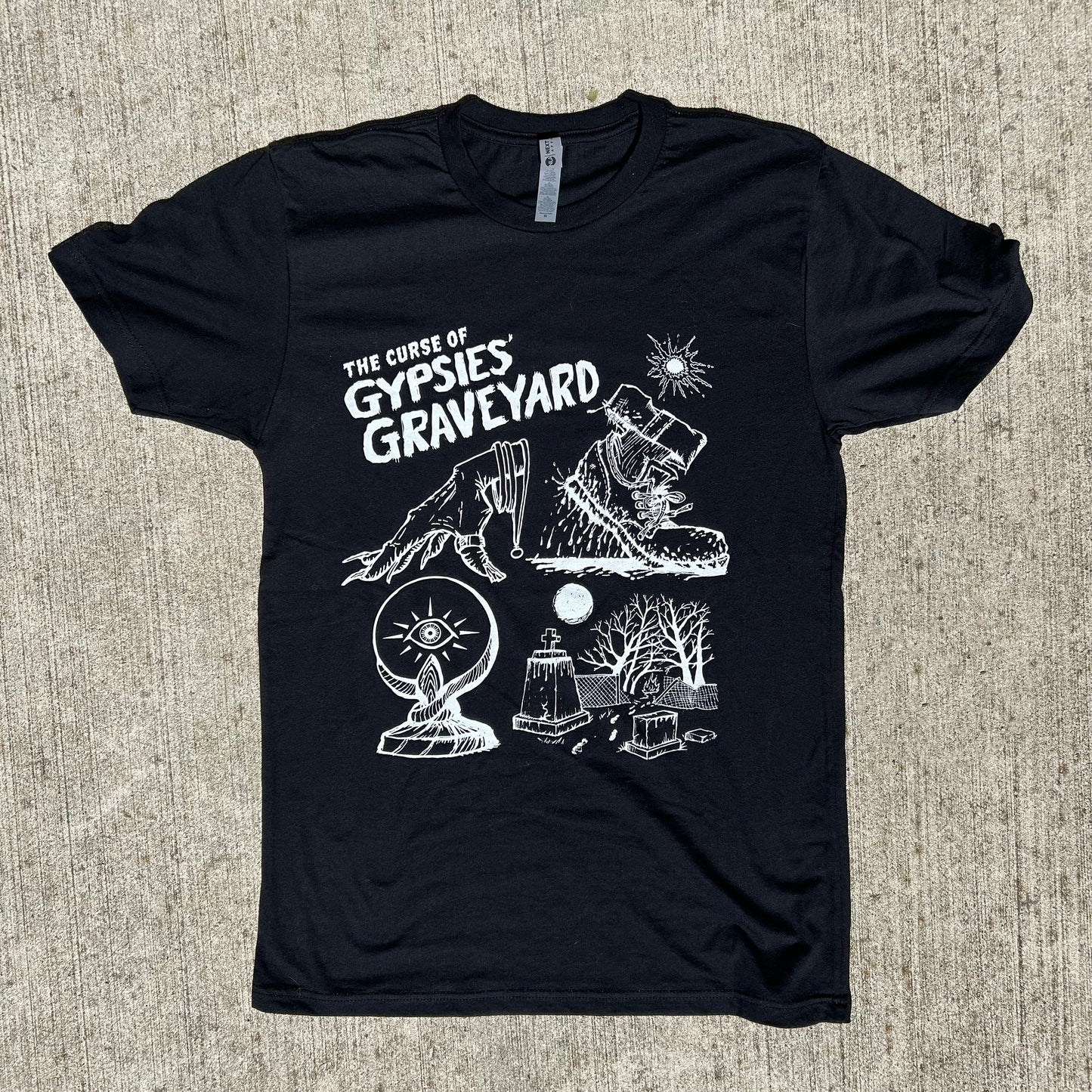 Gypsies Graveyard Indiana paranormal ghost shirt black shirt features white ink art of hand over crystal ball, blood soaked shoe and graveyard with destroyed fence says "the curse of gypsies graveyard", short sleeve crew neck shirt on concrete background