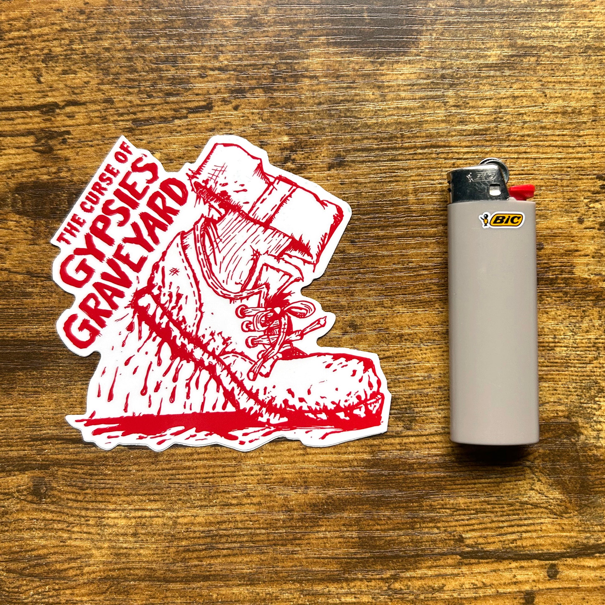 ypsies Graveyard Indiana Sticker indiana ghost indina folklore sticker features bllody shoe, white shoe red blood. Die cut sticker on wood table says "the curse of gypsies graveyard" next to ray bic lighter