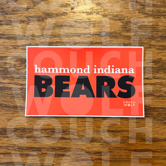 A rectangular orange sticker with a white border featuring the text 'hammond indiana BEARS' in navy blue and black, placed on a brown wood-grain surface. A faint Couch Wolf watermark is visible across the image.