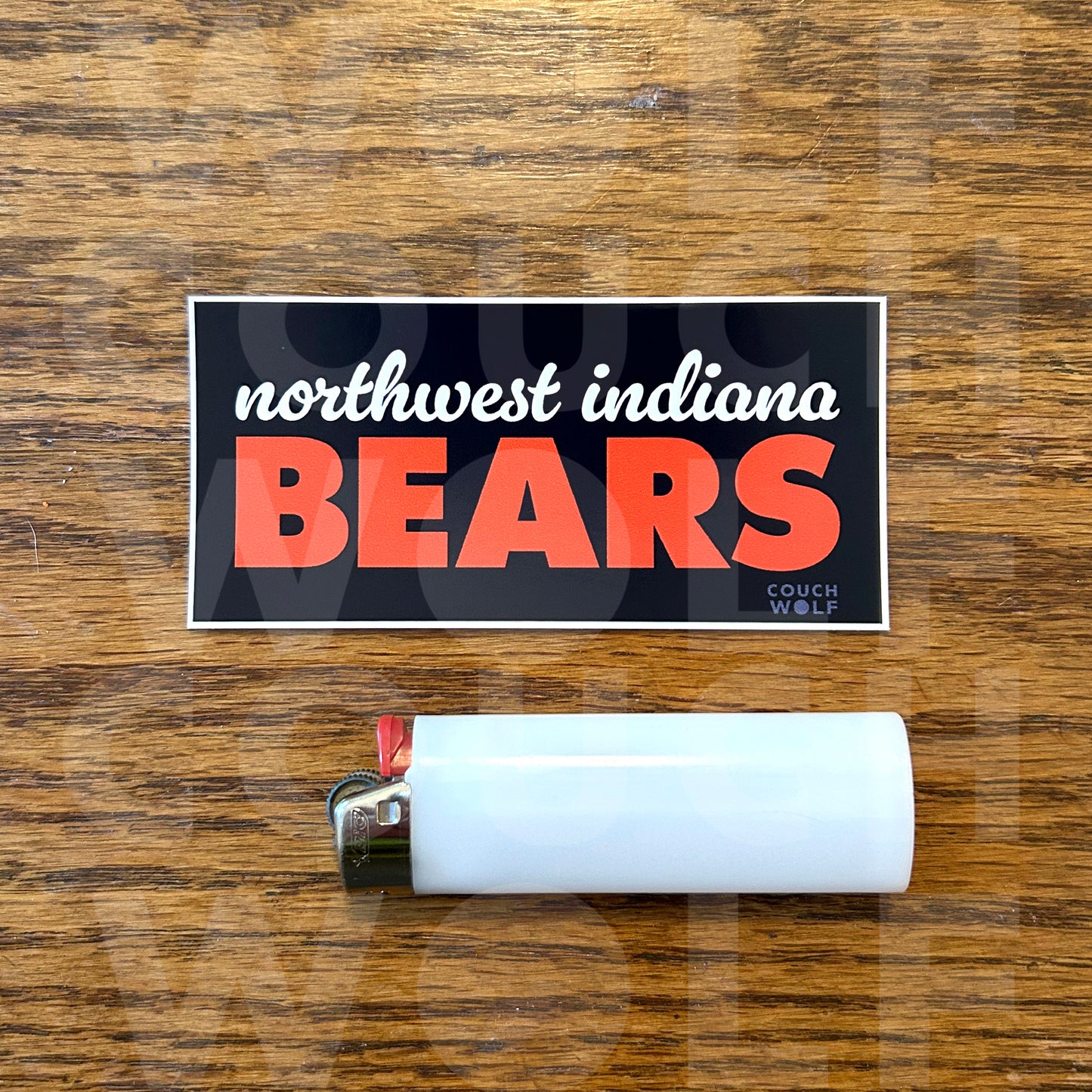 A rectangular sticker reading 'northwest indiana BEARS' with a navy blue background, white script text, and large orange block letters, placed on a wooden surface above a white lighter.