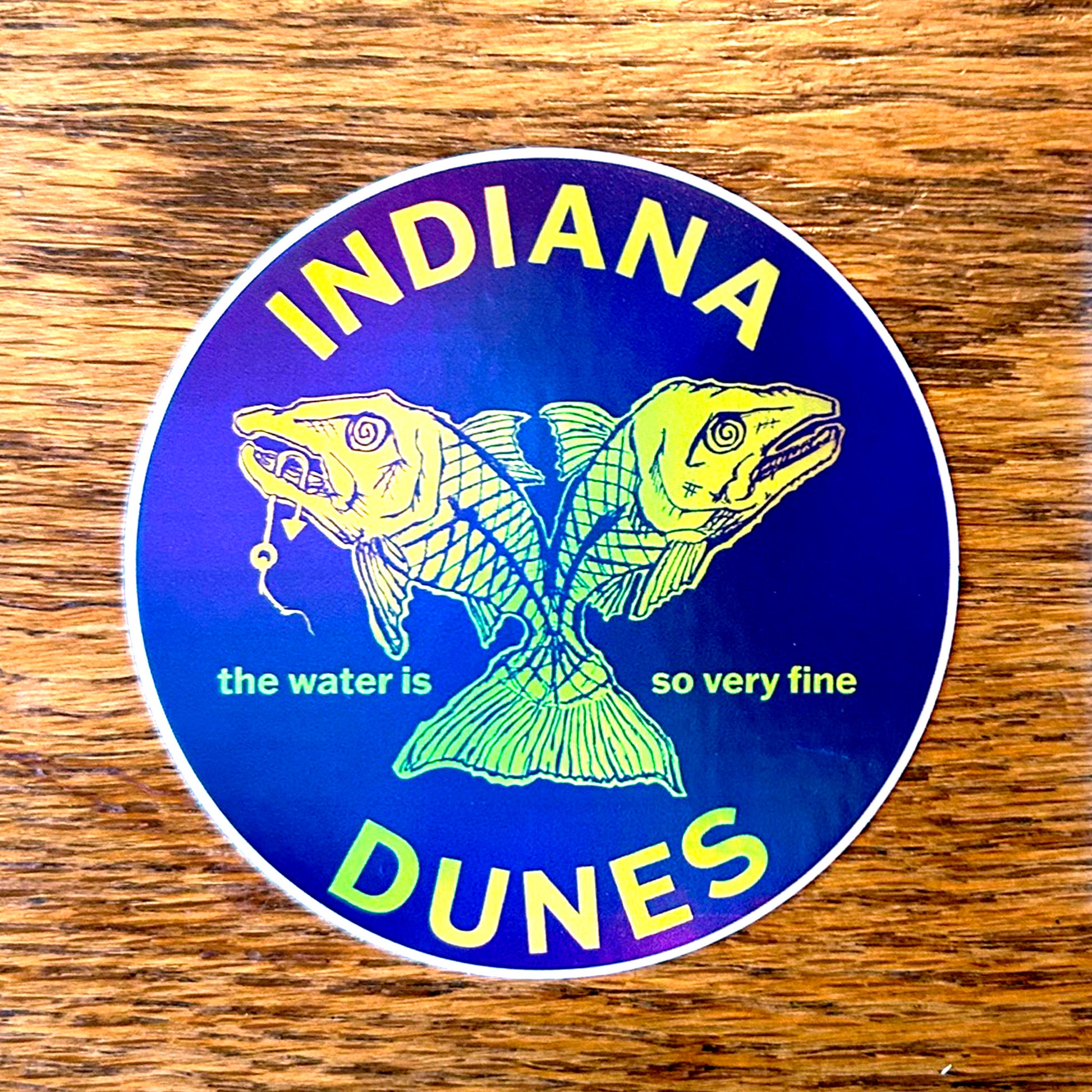 Sticker with fish illustration and 'Indiana Dunes' text on a wooden surface