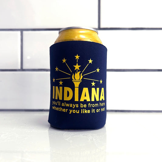 Navy blue can cooler with yellow text and design on a white surface with tiled background says "Indiana you'll always be from here whether you like it or not."