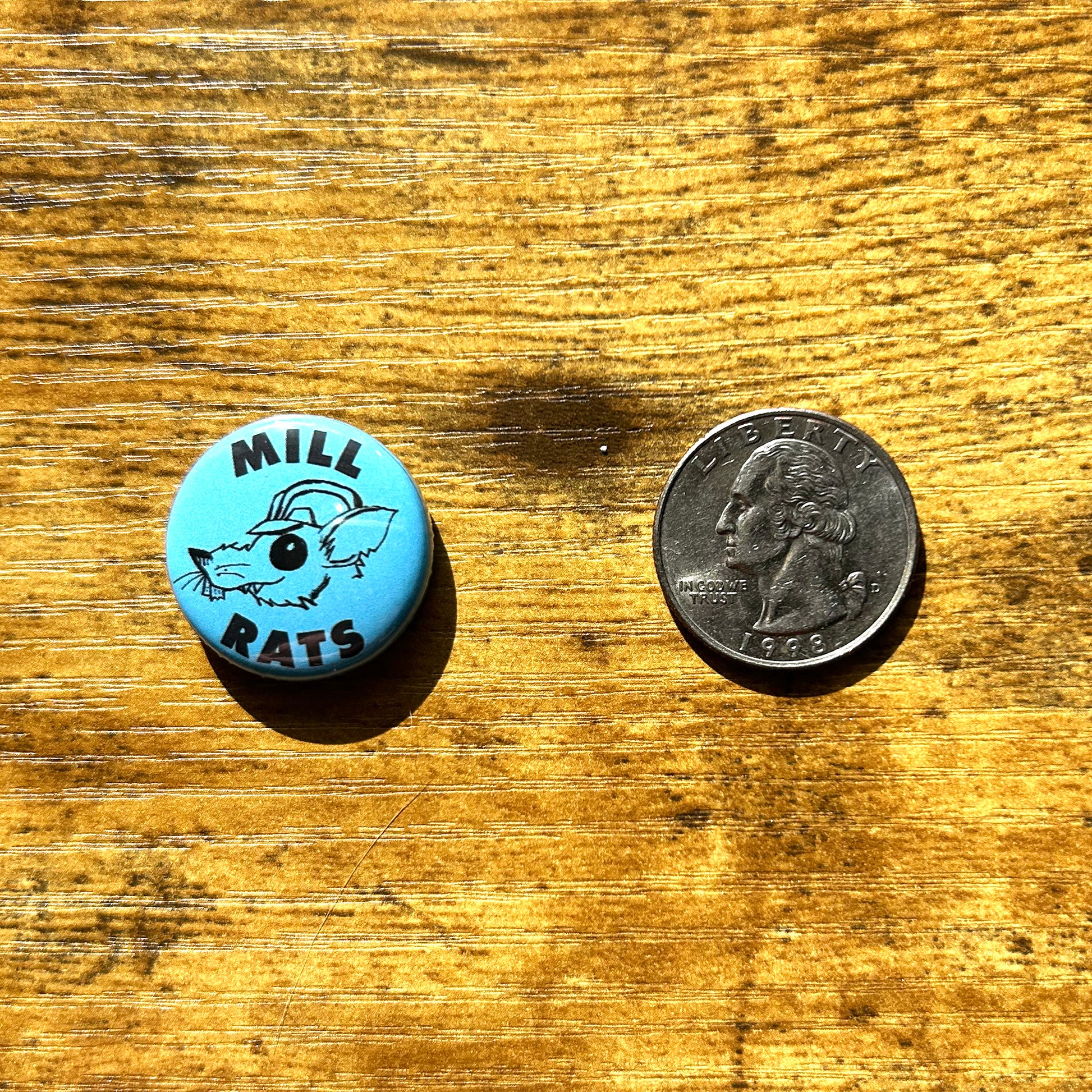 Blue Mill Rat pin next to quarter on wood table