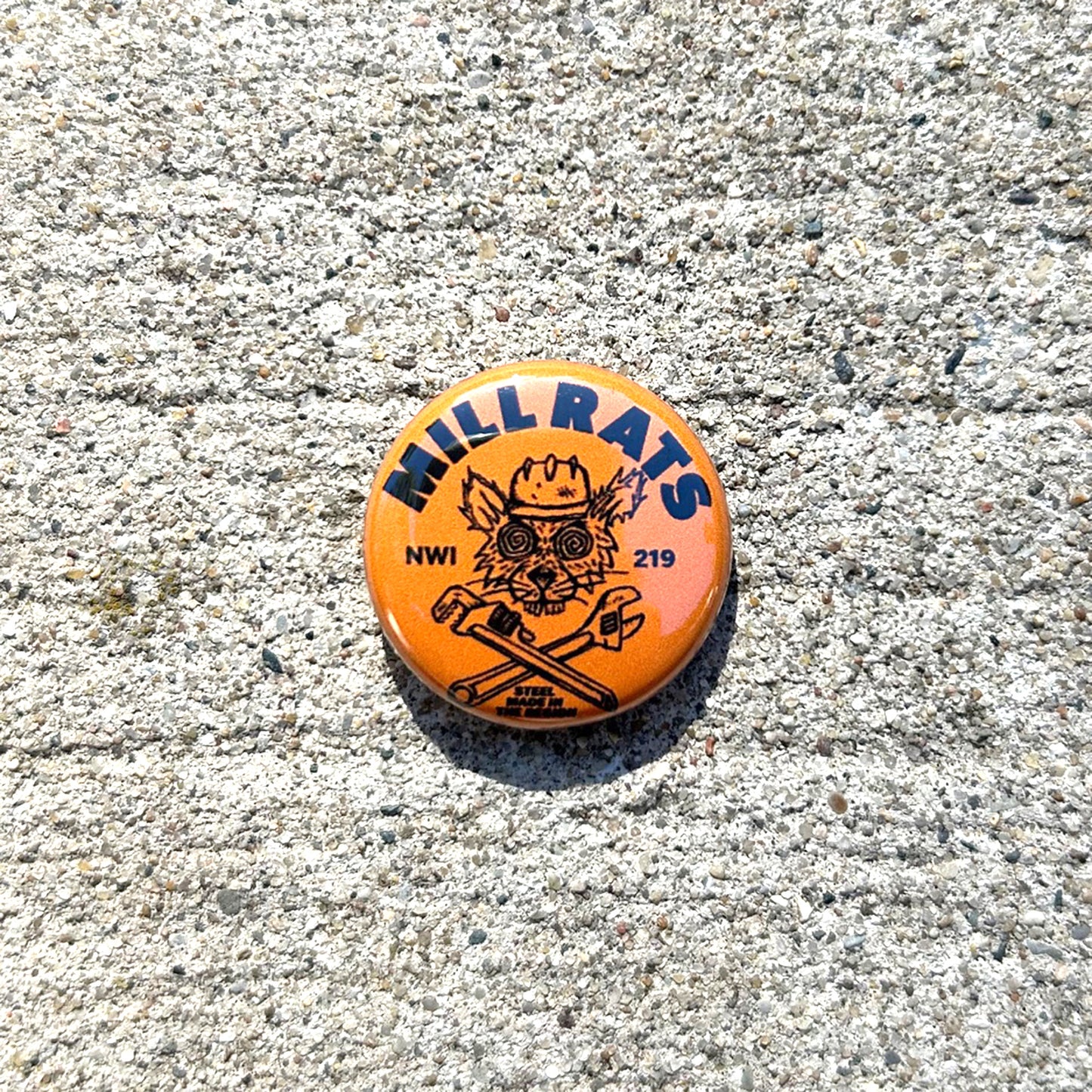 Round button with 'Mill Rats NWI 219' text and graphics on a concrete surface