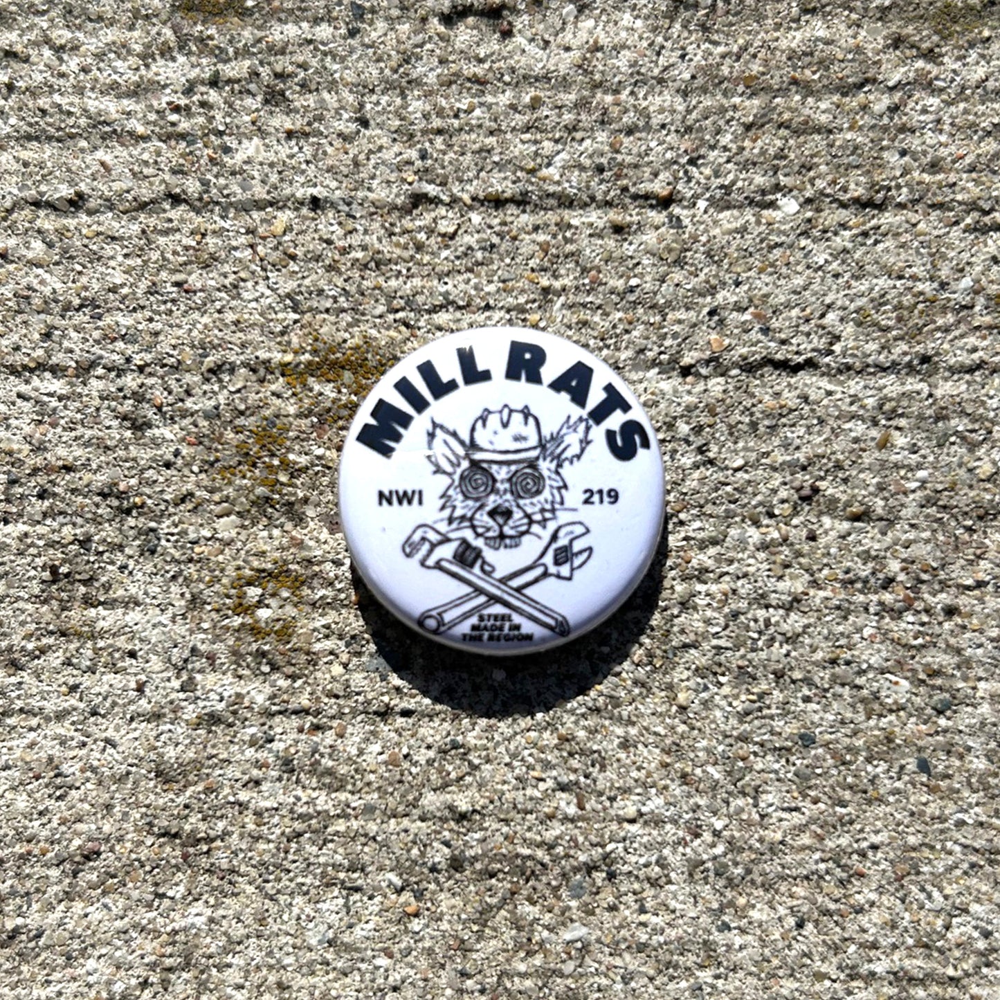 Round white button with 'MILL RATS' logo on a concrete surface