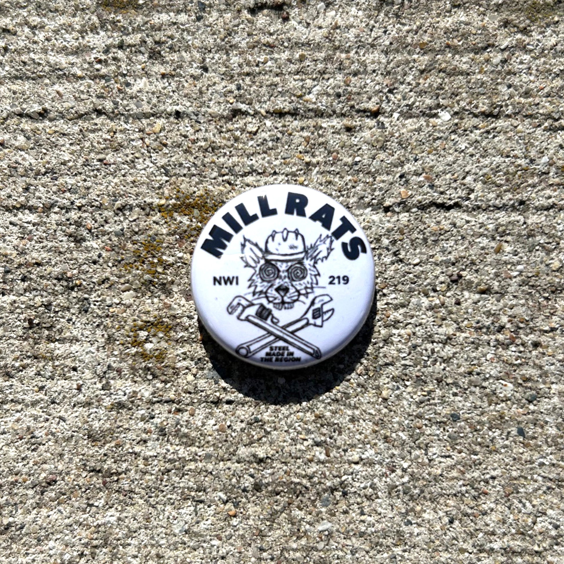 Round white button with 'MILL RATS' logo on a concrete surface