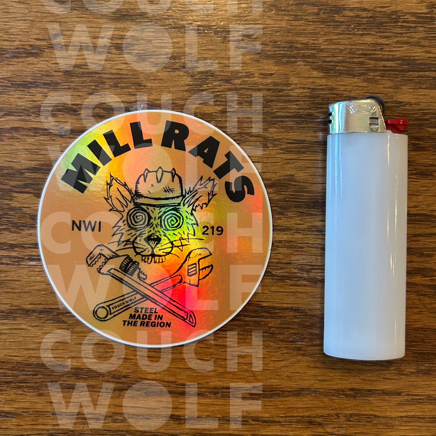 A round sticker featuring a grizzly bear wearing a hard hat with the text 'MILL RATS' and 'NWI 219', shown next to a white lighter on a wooden surface. A faint watermark 'COUCH WOLF' is visible across the image.