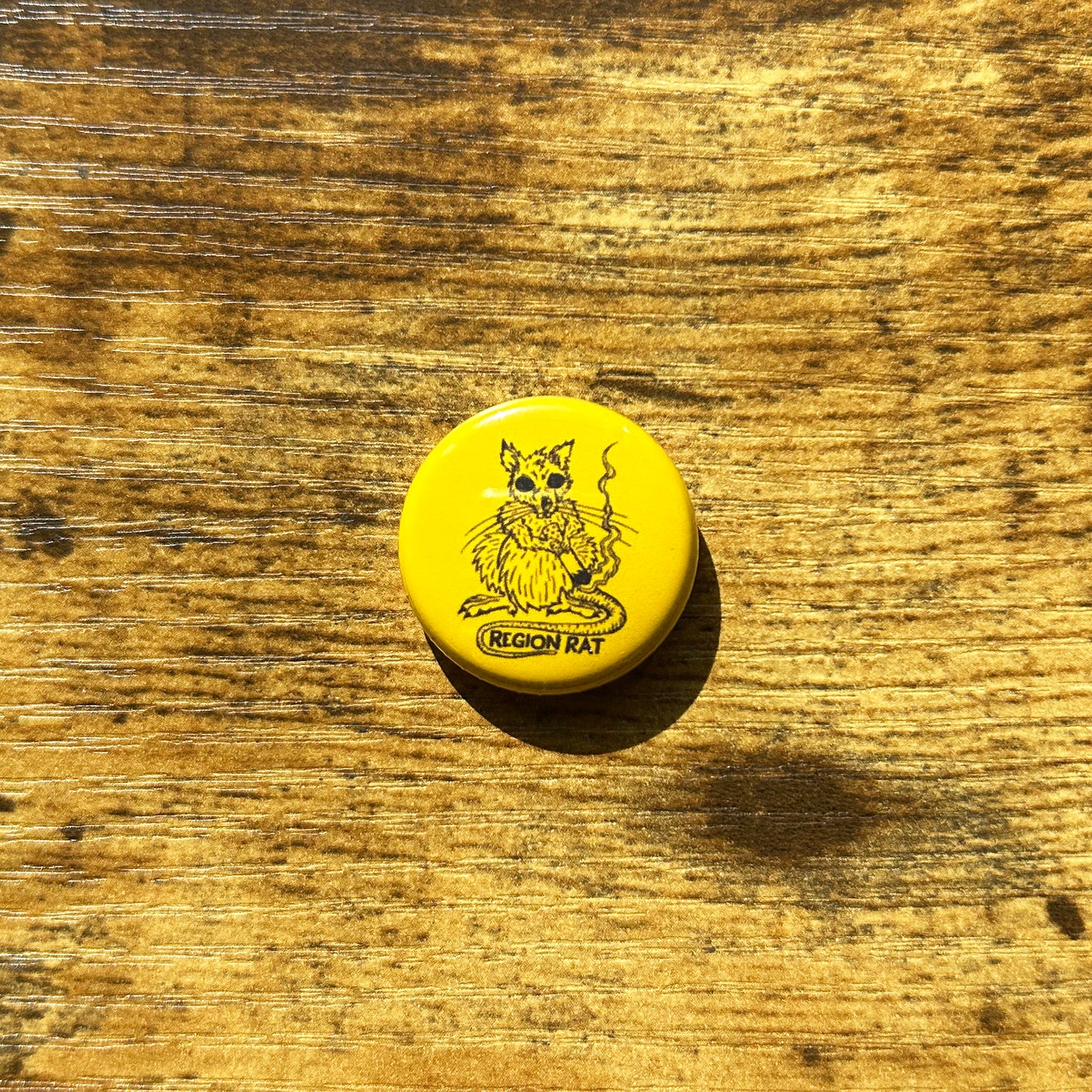 Yellow circle pin on wood table with Region Rat smoking a cigarette dark blue line art artwork