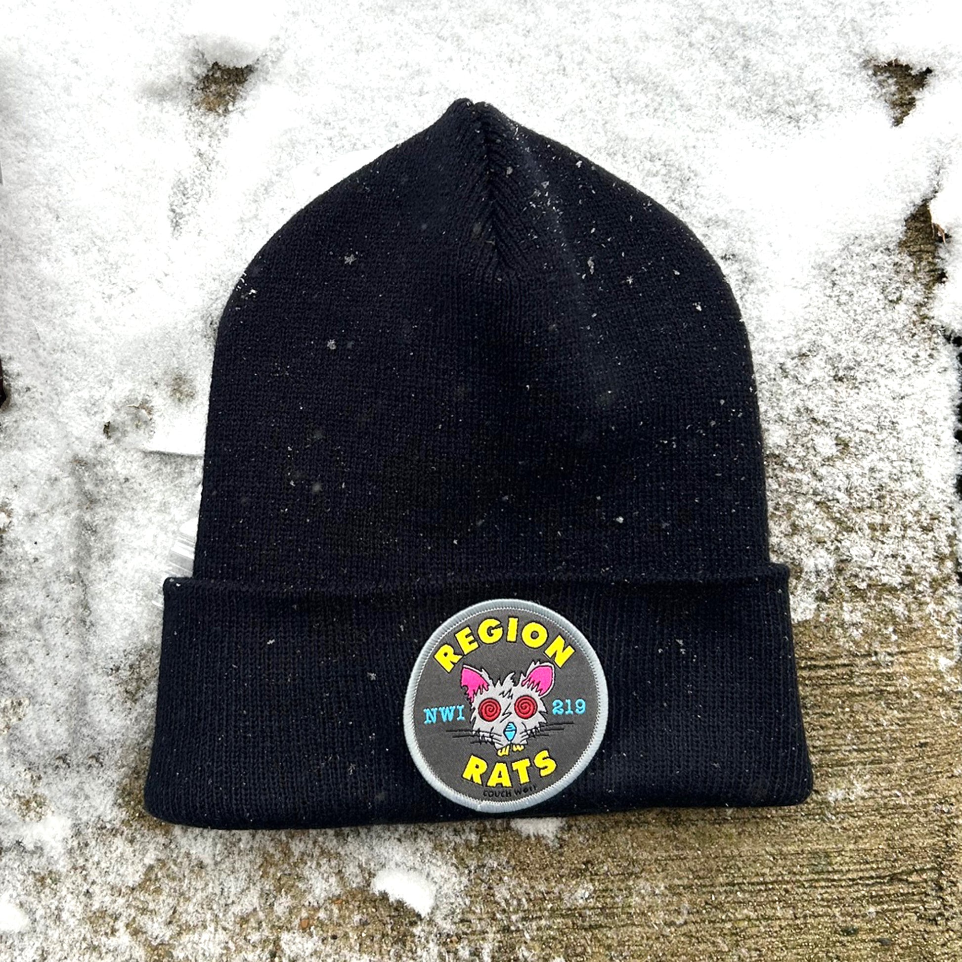 Black beanie with a colorful Region Rats patch on a snowy surface
