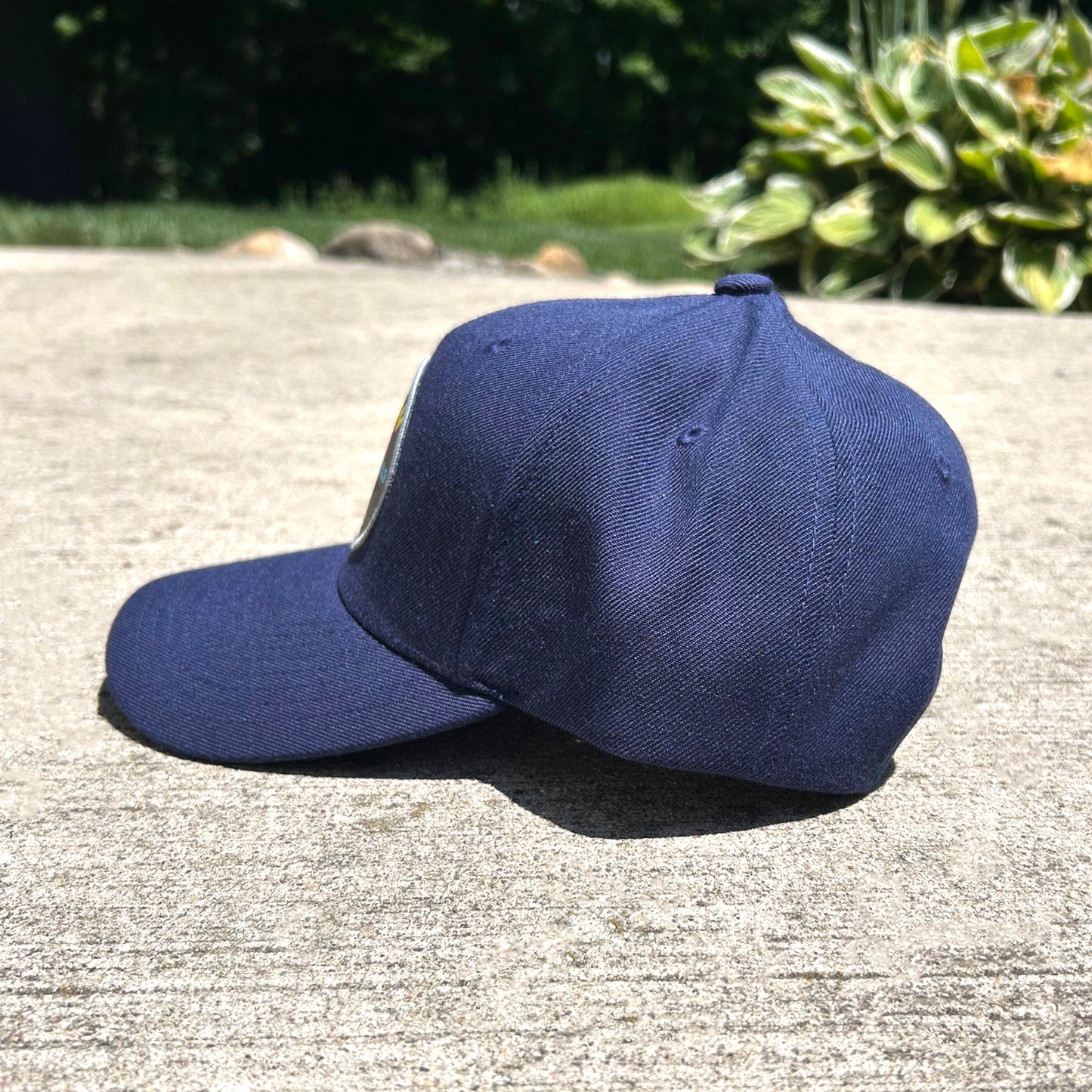 A navy blue baseball cap resting on a concrete surface outdoors, with green foliage in the background.