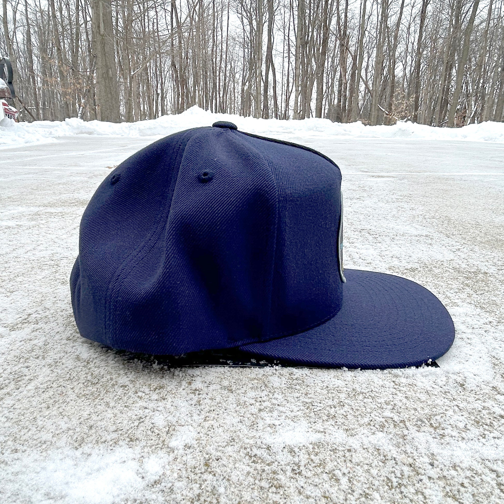 Blue baseball cap on a snowy ground with trees in the background