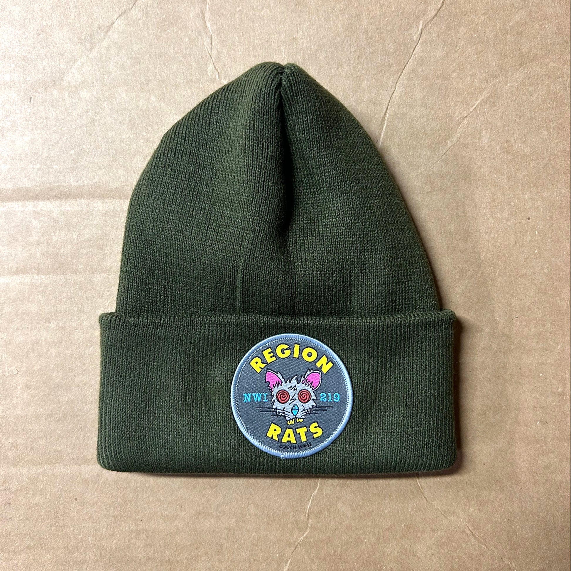 Green region rat beanie with a colorful patch on a beige background