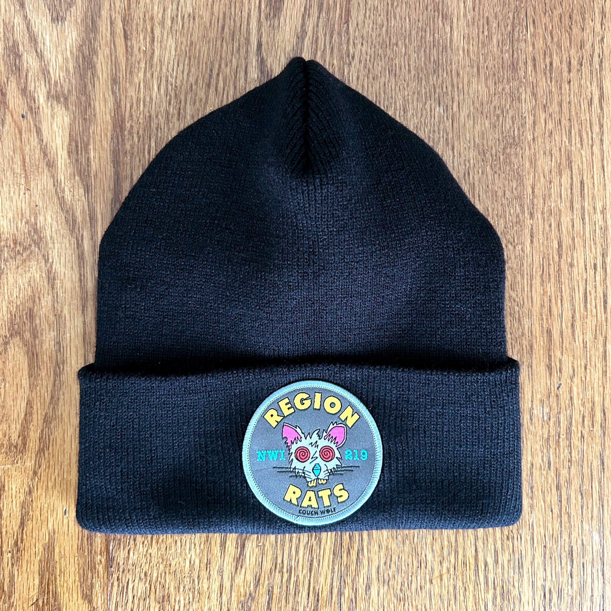 Black  beanie with a circular patch Region Rats patch featuring a rat illustration on a wooden surface