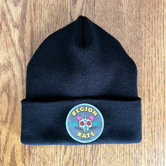 Black  beanie with a circular patch Region Rats patch featuring a rat illustration on a wooden surface