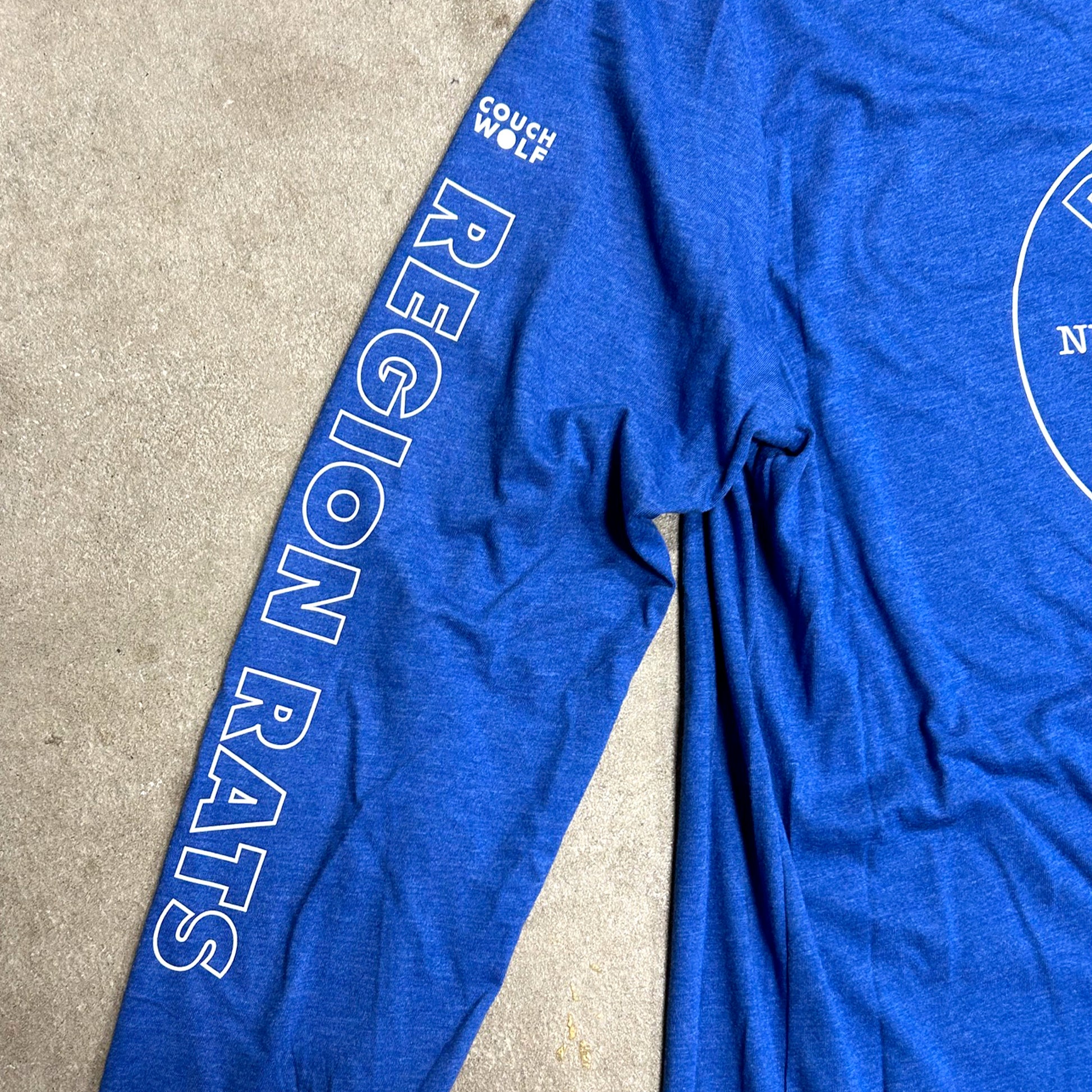 Blue t-shirt with Region Rat  text and Couch Wolf logo on a beige surface