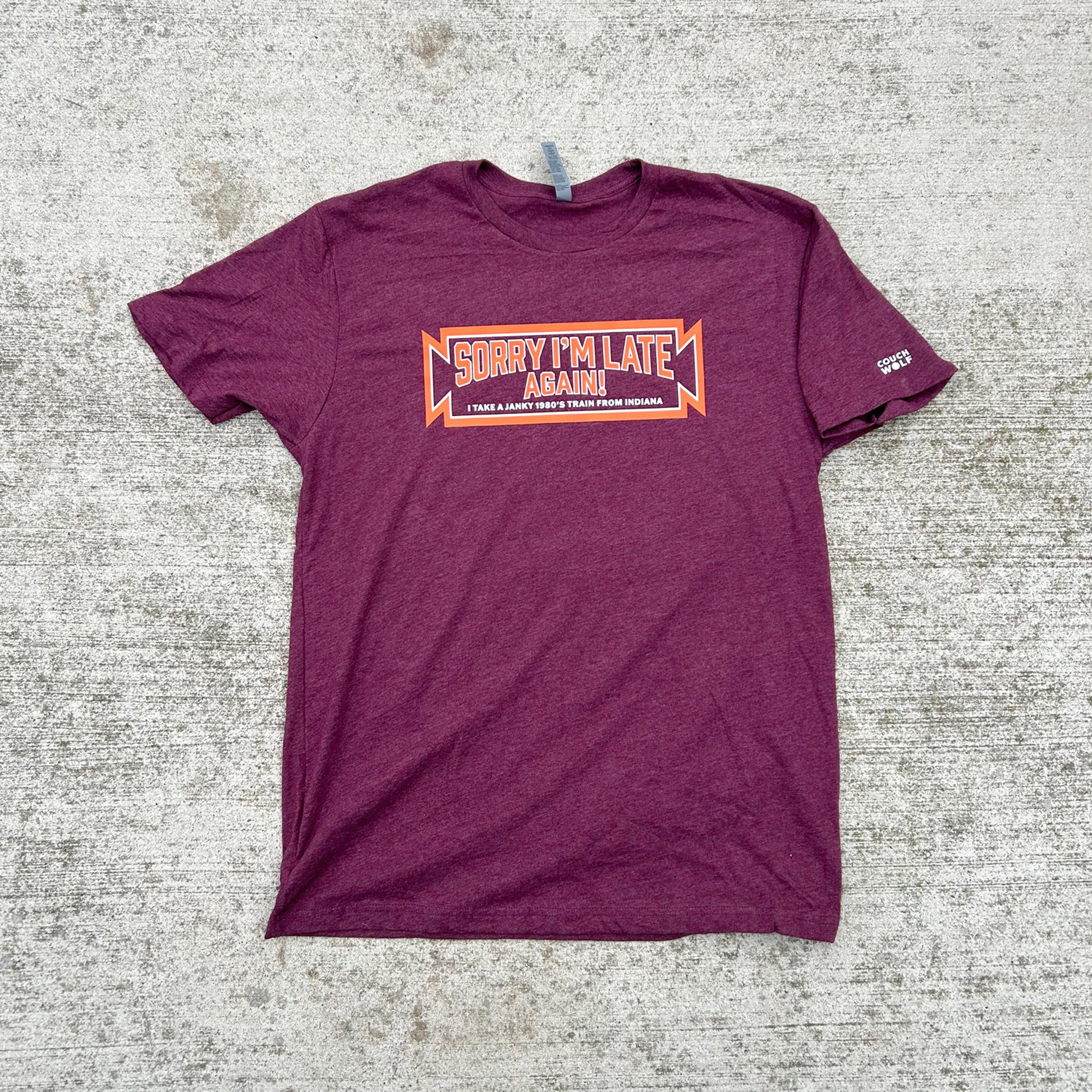 Maroon t-shirt with 'Sorry I'm Late Again' text on a textured surface