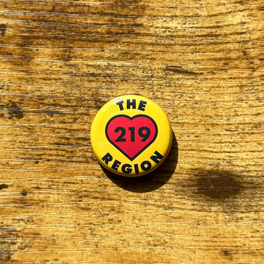 The Region 219 heart pin yellow pin with black letter that say the region 219, 219 is inside of red heart, circle pin shown on wood grain table
