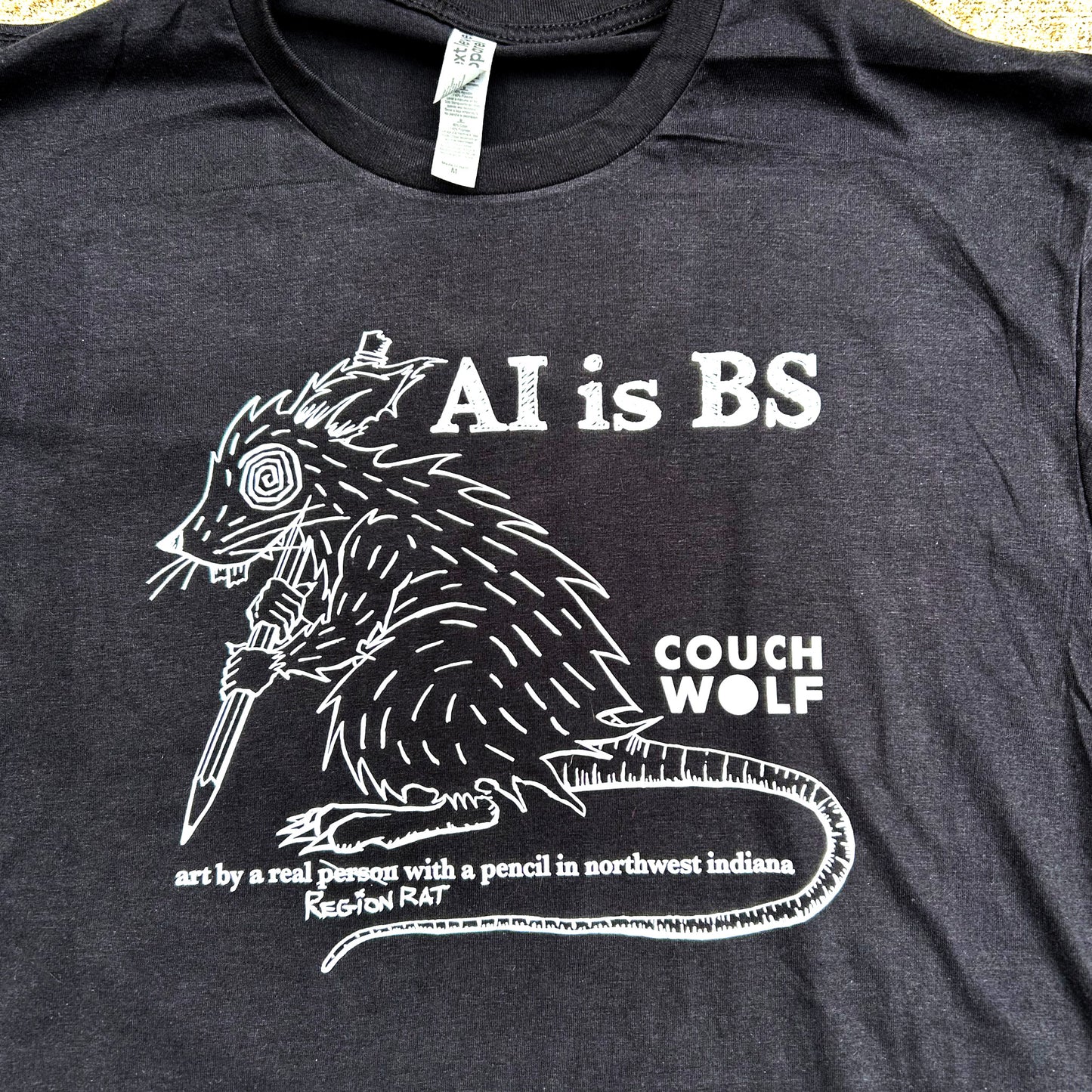 Black t-shirt with white graphic and text 'AI is BS Couch Wolf art by a real person with a pencil' on a plain background