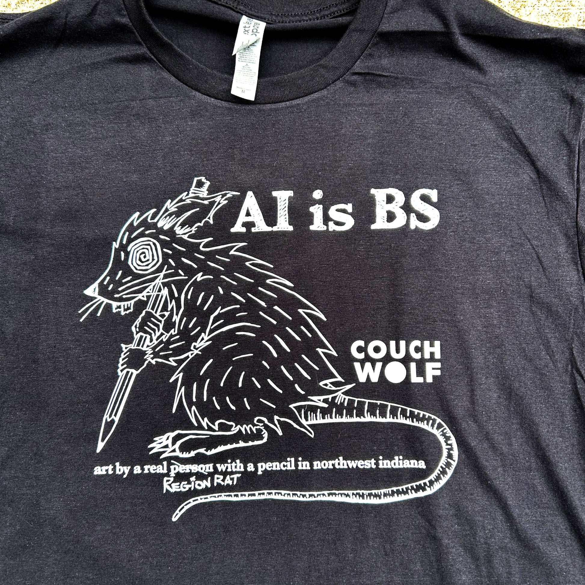 Black t-shirt with white graphic and text 'AI is BS Couch Wolf art by a real person with a pencil' on a plain background