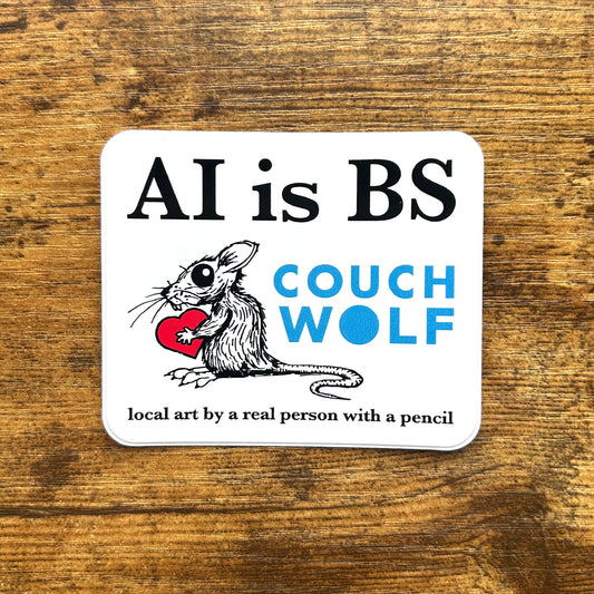 A square white sticker with rounded corners lies on a rustic brown wooden surface. The sticker features the text 'AI is BS' in black, an illustration of a black-and-white rat holding a red heart, the words 'COUCH WOLF' in blue, and the phrase 'local art by a real person with a pencil' in black at the bottom.